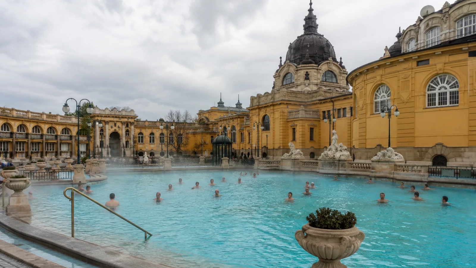 Szabadtéri termálmedencék és történelmi oszlopsor egy budapesti fürdőben.
